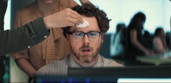 Stressed office worker being handed a tissue while working at computer in Globant commercial