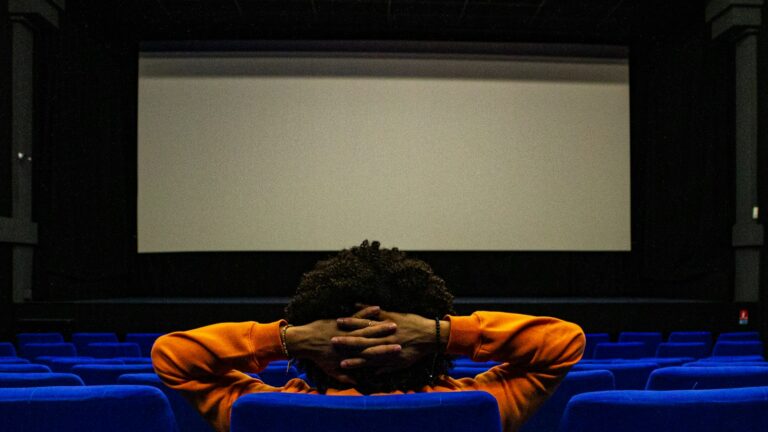 A viewer in an orange jacket sits alone in a cinema in front of a blank screen